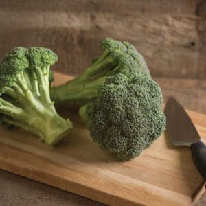 Two broccoli heads on cutting board with knife