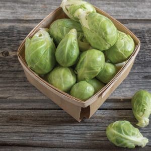 Basket of fresh green Brussels sprouts on a wooden surface.