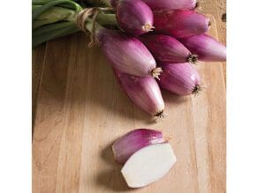 Fresh purple shallots on a wooden surface with one sliced open.