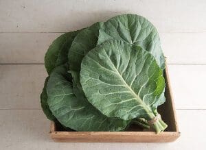 Fresh green collard leaves neatly stacked in a wooden crate.