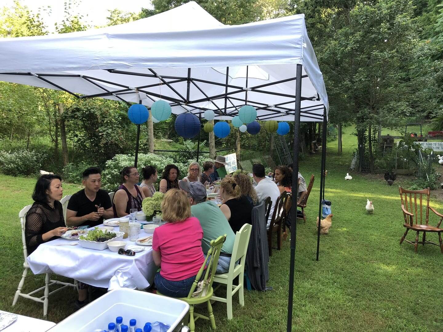 Outdoor gathering under a canopy with people enjoying a meal together.