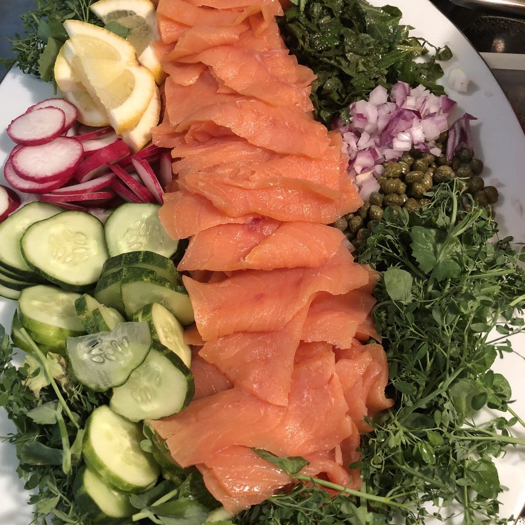 Plate of smoked salmon with fresh vegetables and lemon wedges.