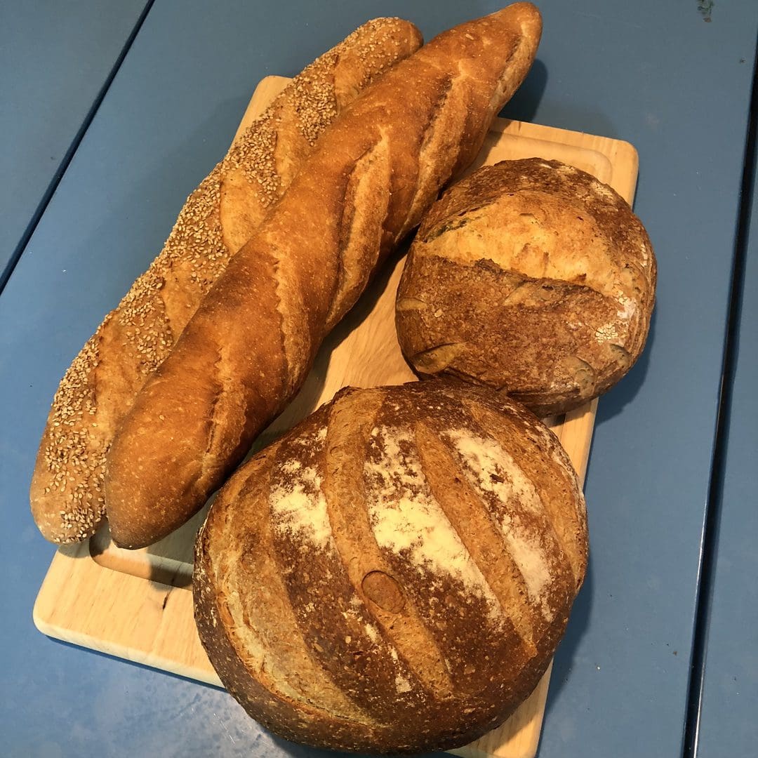 Freshly baked baguette and two round crusty loaves on a cutting board.