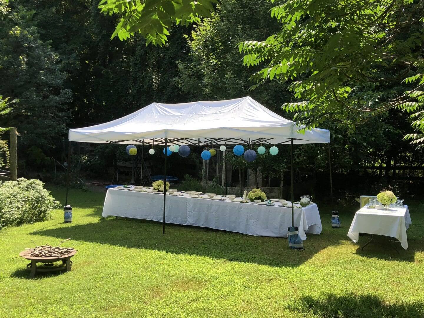 Outdoor event setup with white tents and decorated tables on green grass.