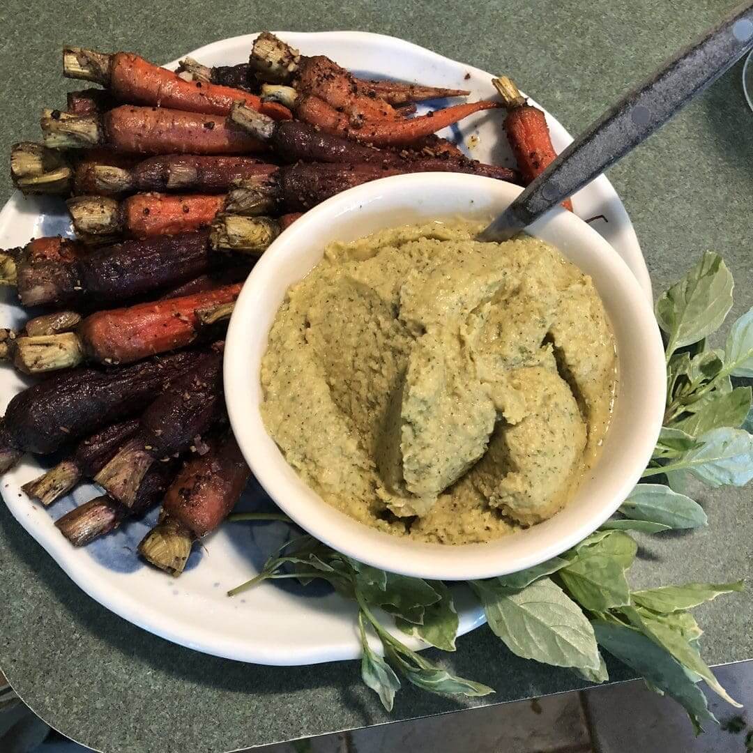 Plate of roasted carrots with a bowl of creamy dip and fresh herbs.