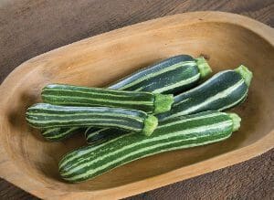 Fresh striped zucchini on a wooden tray.