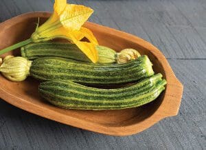 Three striped green zucchinis with a yellow flower on a wooden dish.