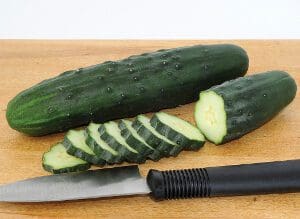 Fresh cucumber with slices and a knife on a wooden board.