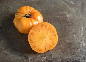 Yellow heirloom tomato, whole and sliced, on a dark surface.