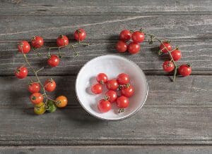 Cherry tomatoes arranged on a wooden surface with some in a white bowl.