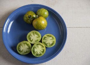 Green tomatoes, whole and sliced, on a blue plate.