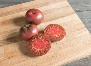 Heirloom tomatoes on a wooden cutting board, one sliced to reveal a vibrant interior.