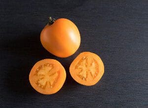 Whole and sliced yellow tomatoes on a dark surface.