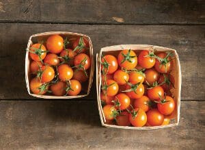 Two baskets filled with fresh cherry tomatoes on a wooden surface.