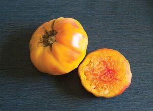 Two yellow-orange heirloom tomatoes, one whole and one sliced.