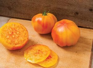 Two whole and sliced yellow tomatoes on a wooden surface.
