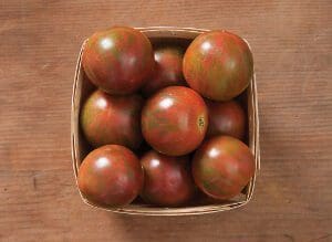 Basket of ripe, dark-colored tomatoes on a wooden surface.