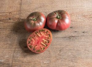 Three ripe heirloom tomatoes on a wooden surface, one sliced open.