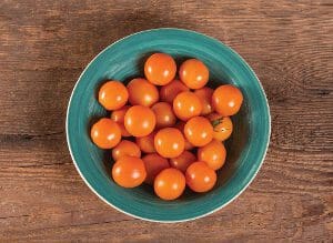 A bowl filled with fresh orange cherry tomatoes on a wooden surface.