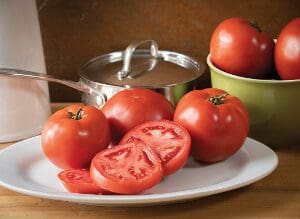 Fresh ripe tomatoes on a plate with a cooking pot in the background.