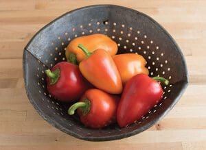 Fresh red and orange peppers in a rustic colander.