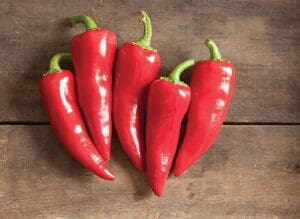 Five fresh red chili peppers on a wooden surface.