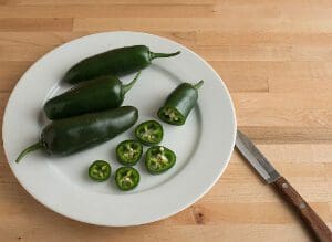 Fresh jalapeño peppers on a white plate with a knife.