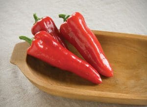 Two red chili peppers on a wooden dish.