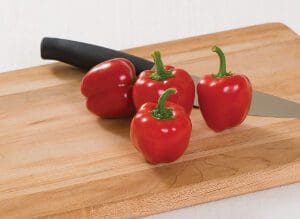 Four red bell peppers on a wooden cutting board with a knife.