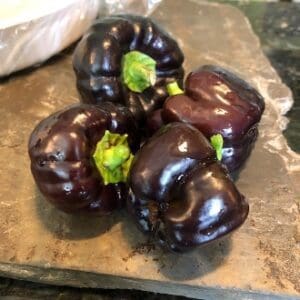Four shiny, dark purple bell peppers on a wooden surface.