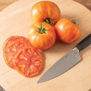 Fresh heirloom tomatoes and a sliced tomato on a wooden cutting board with a knife.