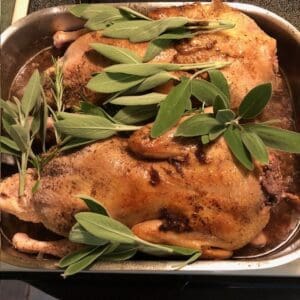 A roasted whole duck garnished with fresh green herbs in a metal tray.