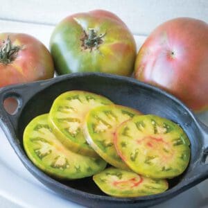 Freshly sliced green heirloom tomatoes in a black pan with whole tomatoes in the background.