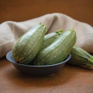 Fresh green zucchinis in a bowl on a wooden table.