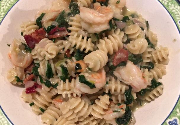 Plate of rotini pasta with shrimp, spinach, and bacon bits.