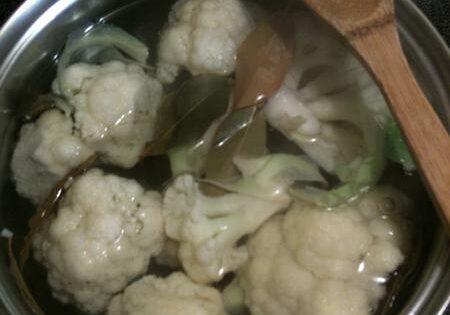 Cauliflower florets boiling in a pot of water with a wooden spoon.